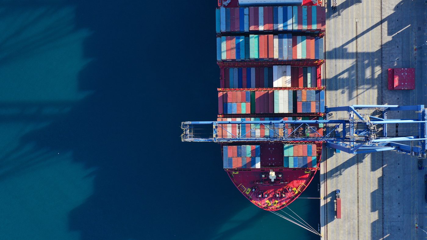 Aerial view of a container ship berthed at a terminal, with cranes reaching over the deck