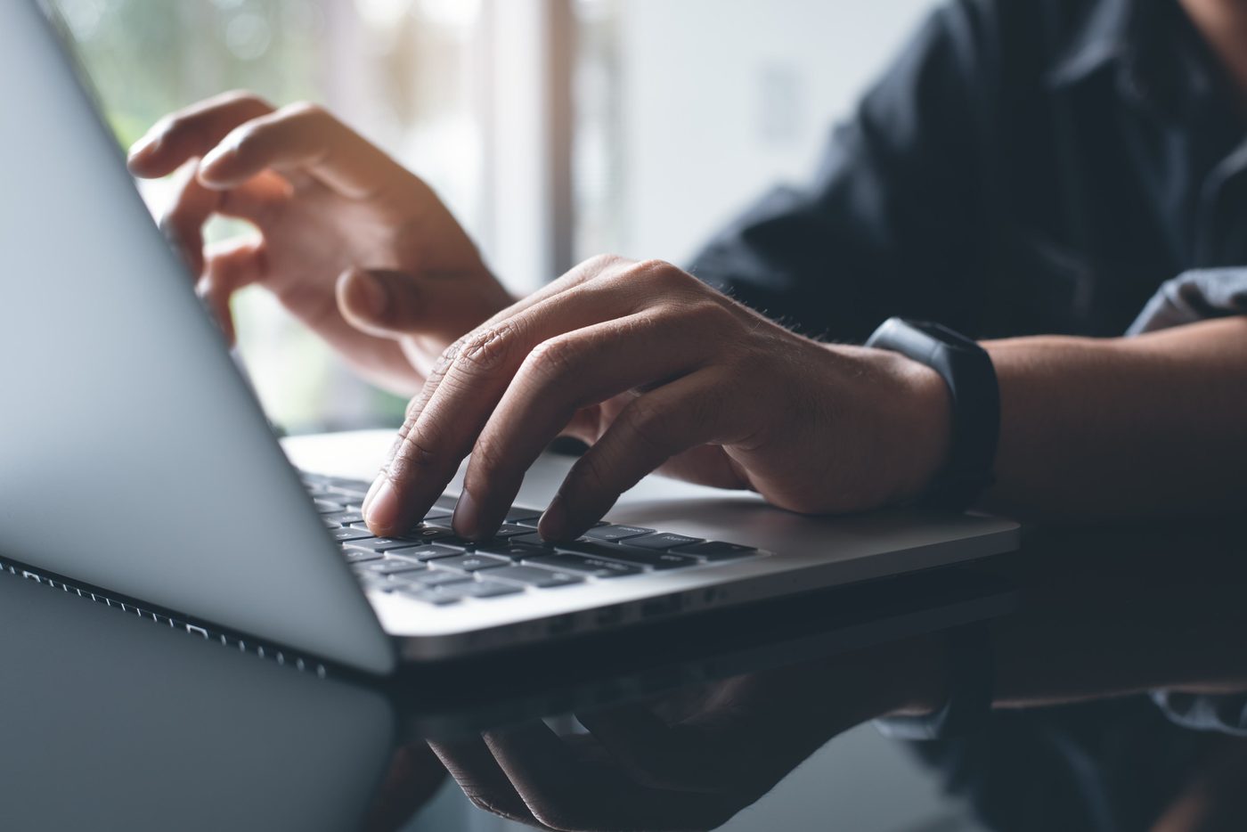 Close-up of hands typing on a laptop keyboard at a desk near a window