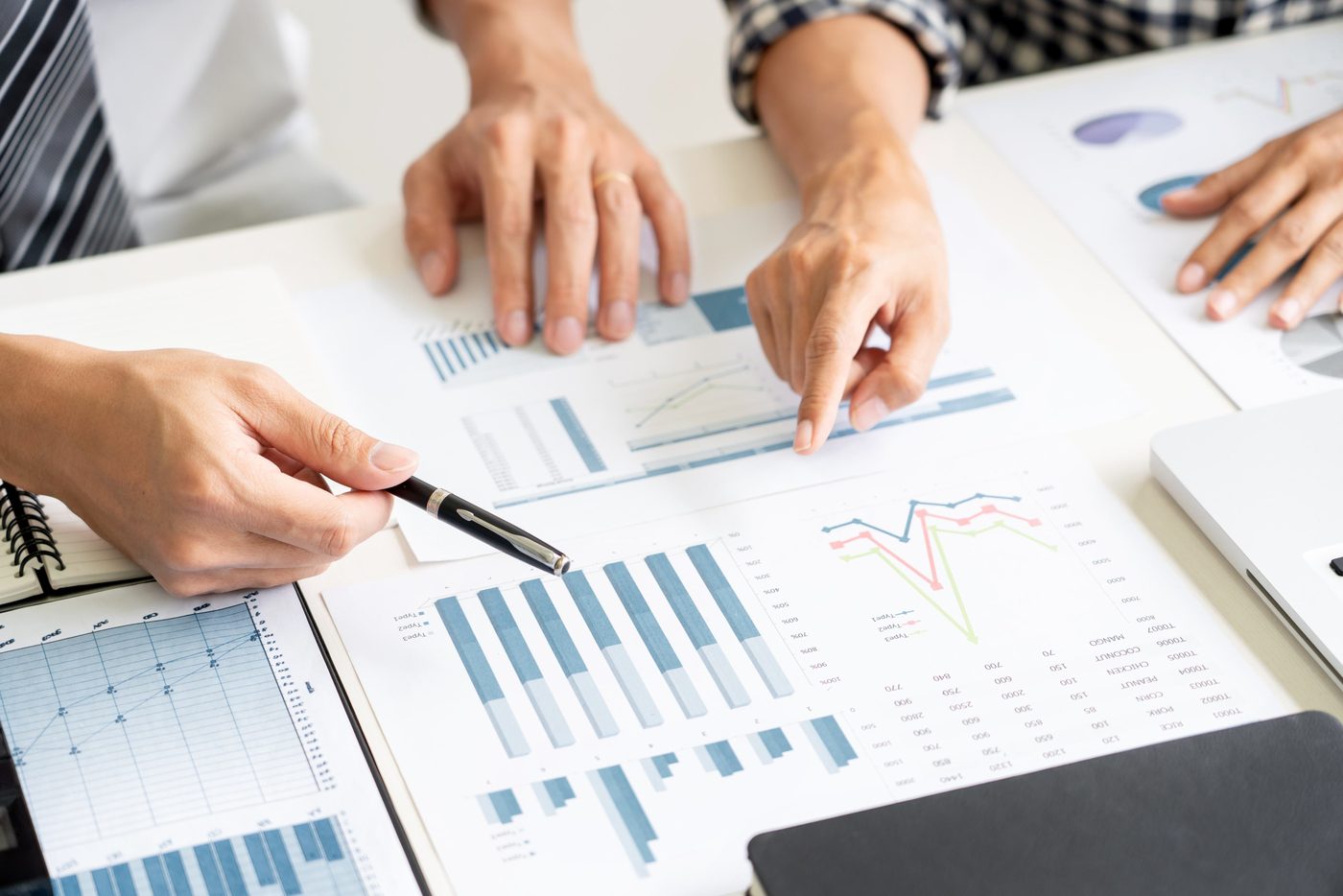 Hands pointing at printed data charts and graphs during a strategy meeting